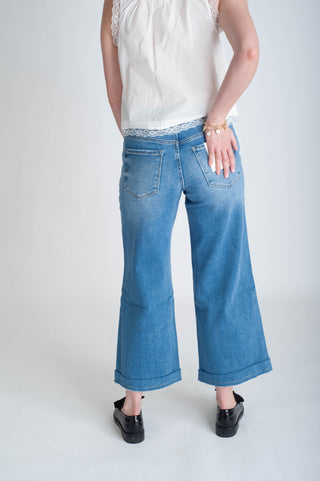 Person wearing blue jeans and a white top on a plain background