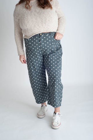 Person wearing a beige sweater and blue polka dot pants on a white background