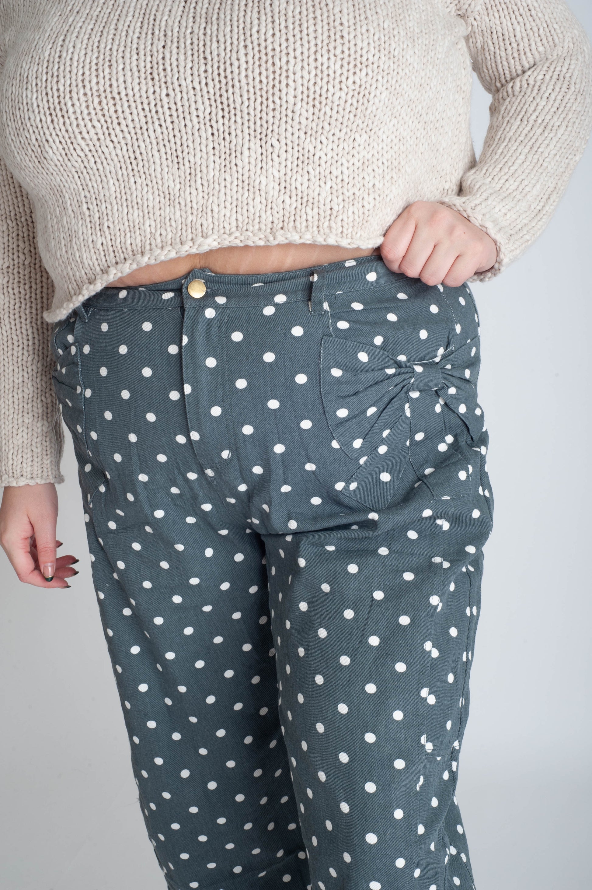 Person wearing a beige sweater and polka dot pants on a plain background