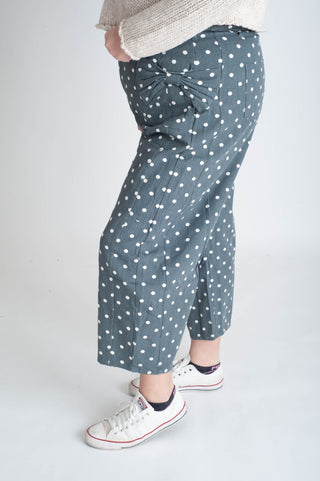 Person wearing blue polka dot pants with white sneakers on a plain background