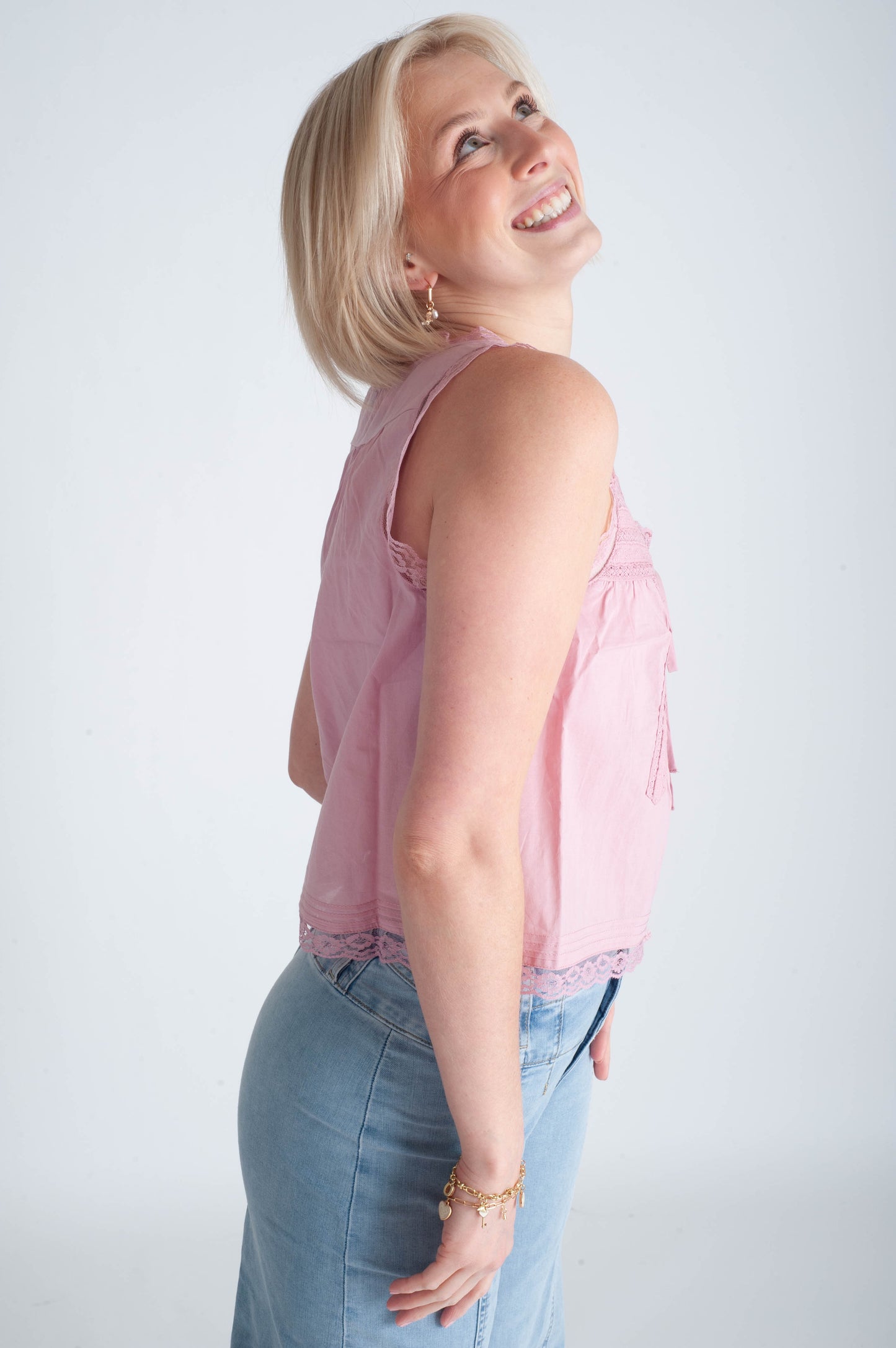 Woman wearing a pink sleeveless top and blue jeans against a white background