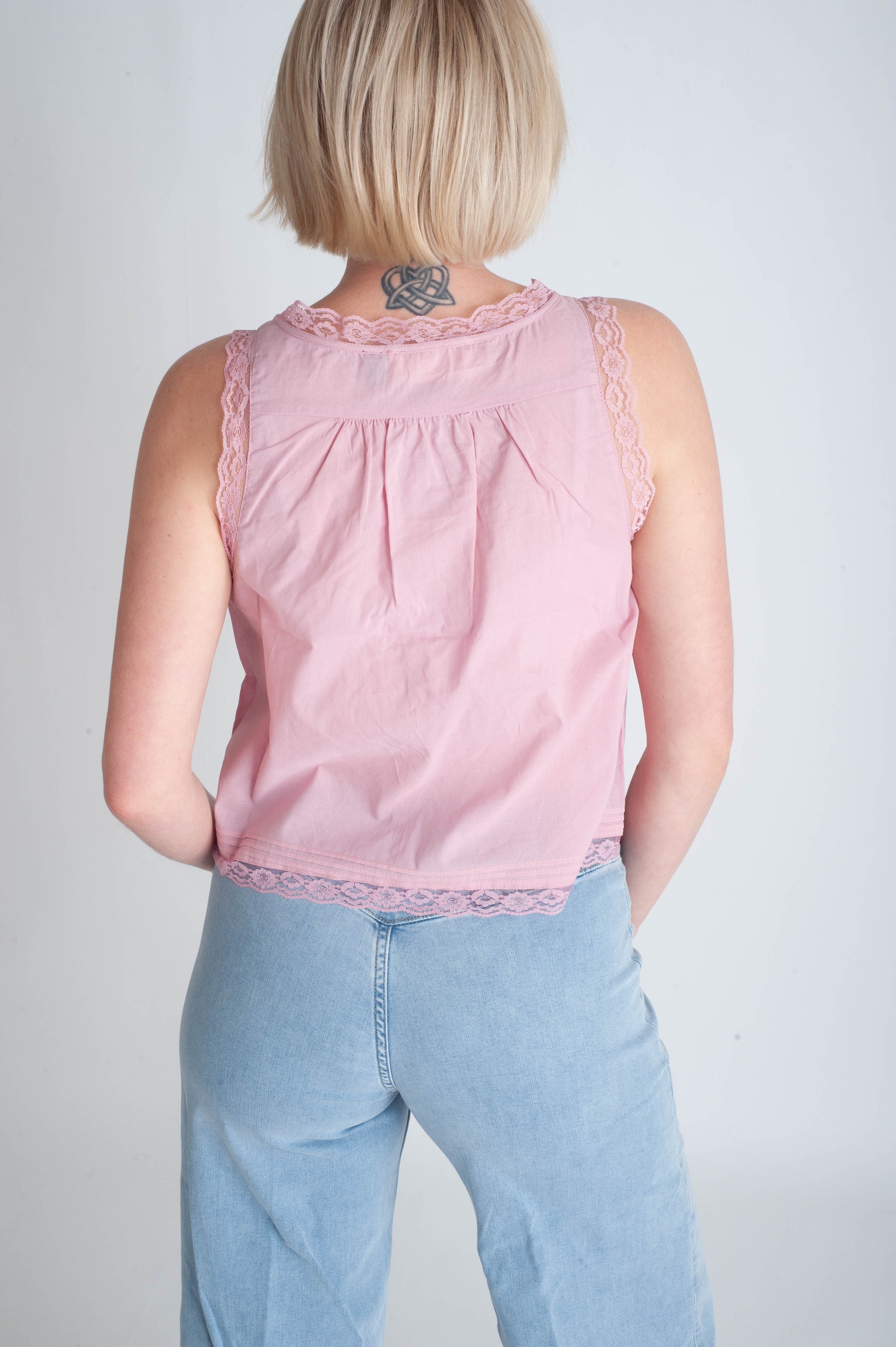 Person wearing a pink sleeveless top and light blue jeans against a plain background