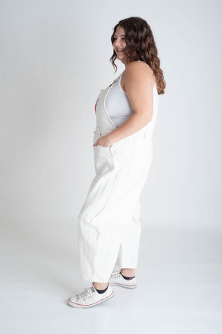 Woman wearing a white dress with a patterned strap against a plain background