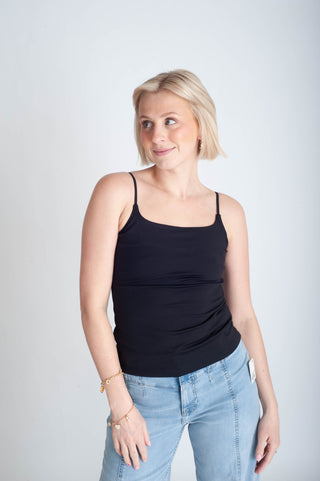 Woman wearing a black tank top and light blue jeans against a plain background