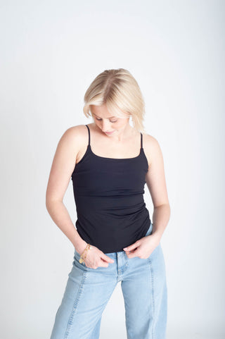 Woman wearing a black tank top and light blue jeans on a white background