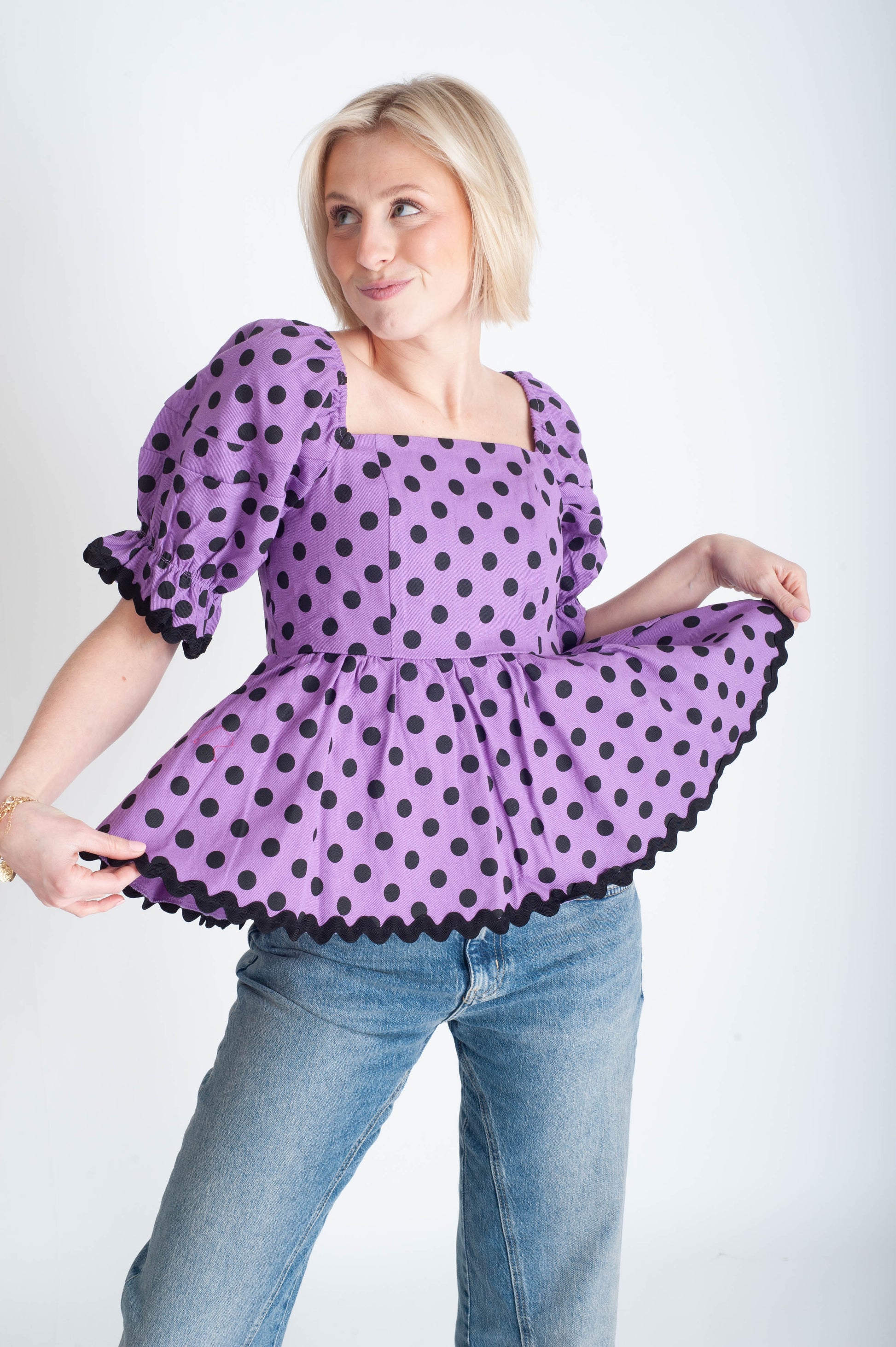Woman wearing a purple polka dot blouse and jeans on a white background