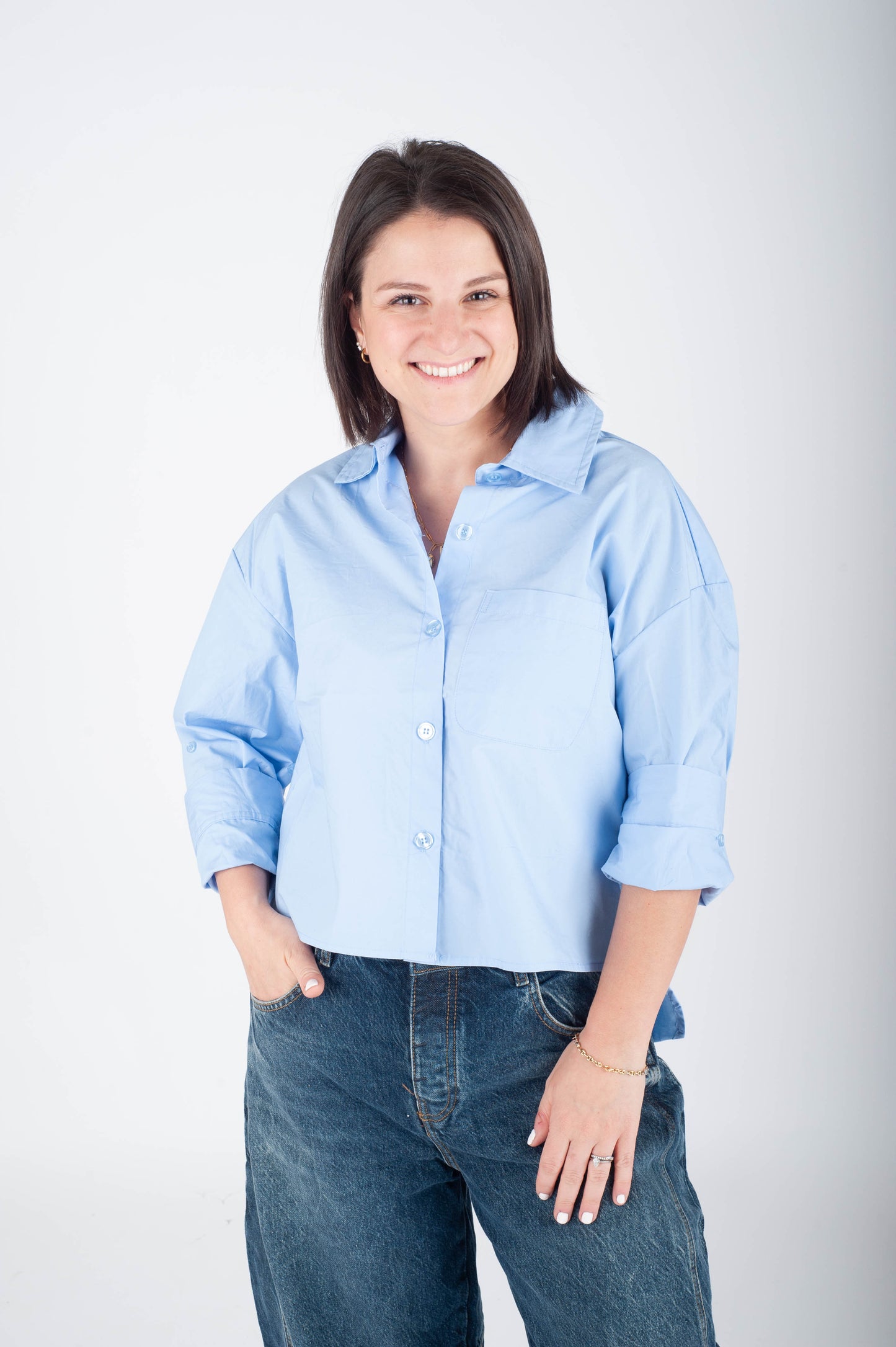 Woman wearing a light blue shirt and dark jeans against a white background