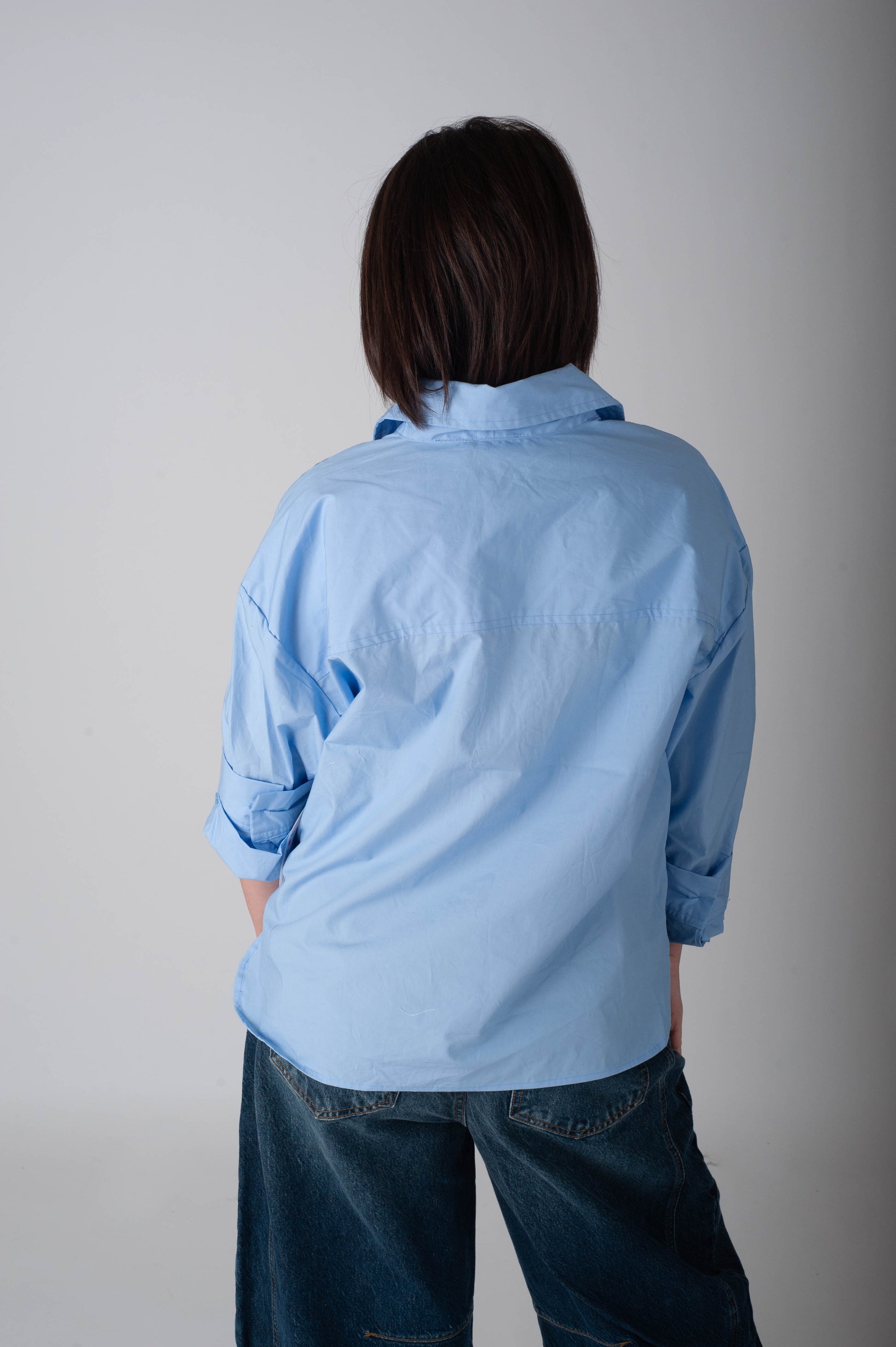 Person wearing a light blue shirt and dark jeans against a plain background