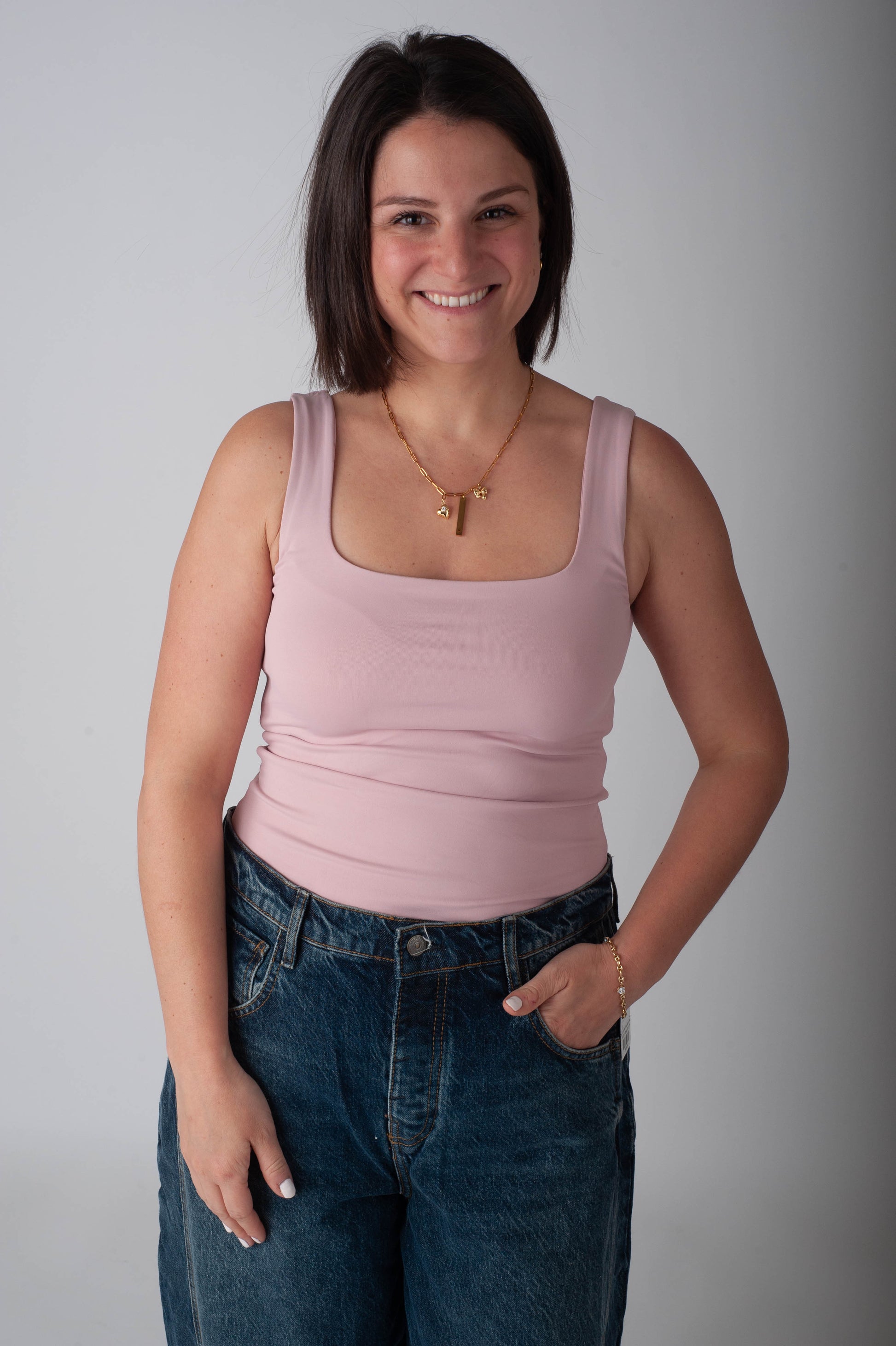 Woman wearing a pink tank top and blue jeans against a plain background