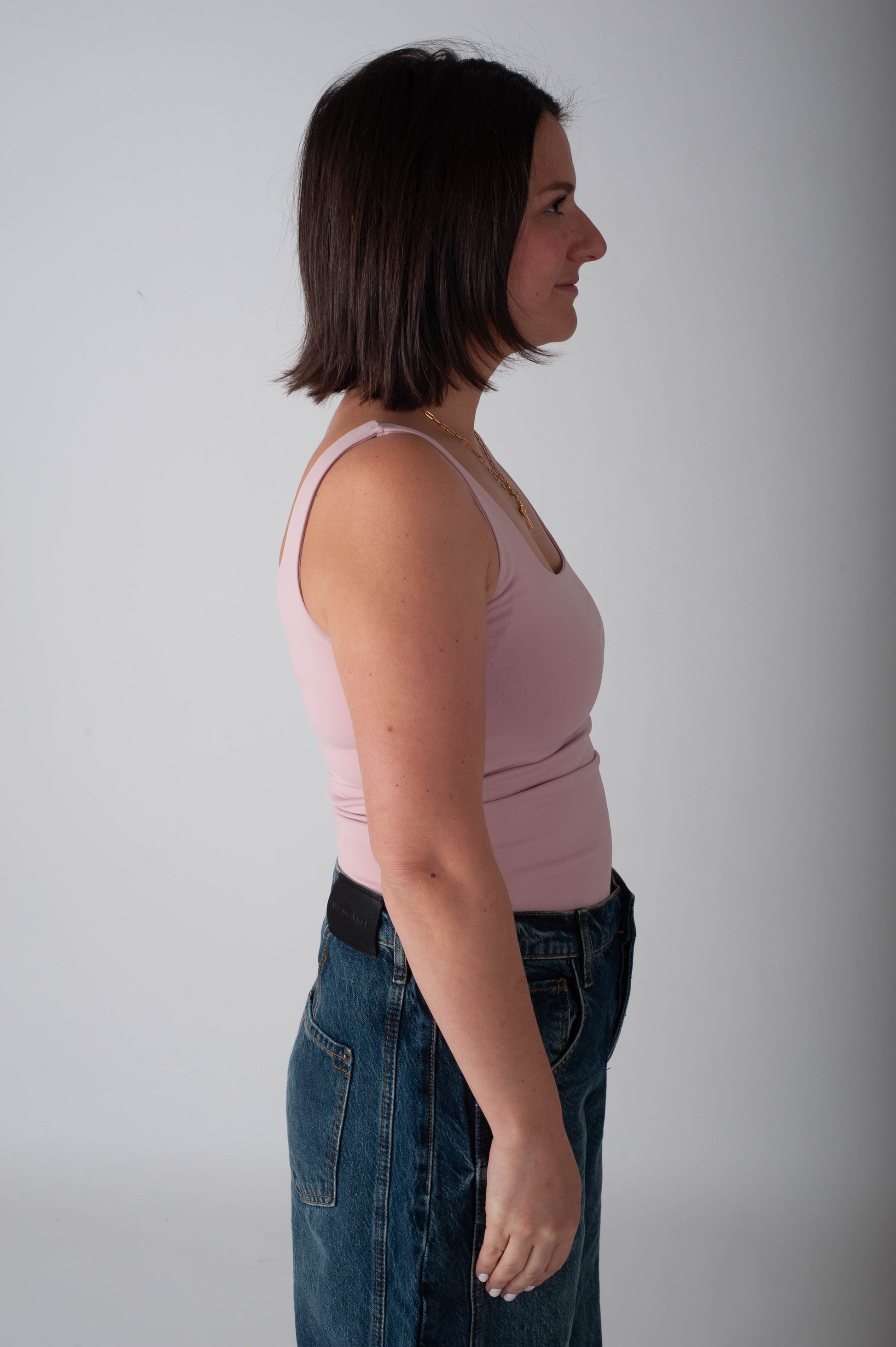 Woman wearing a pink tank top and blue jeans against a plain background