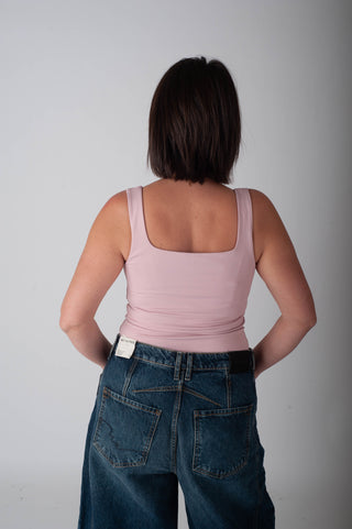 Person wearing a pink tank top and blue jeans against a plain background