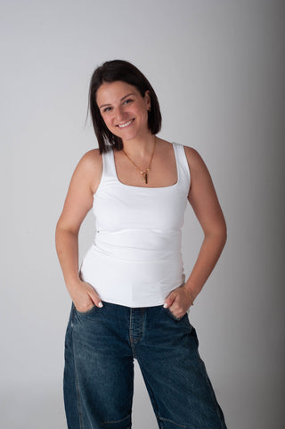 Woman wearing a white tank top and blue jeans against a gray background