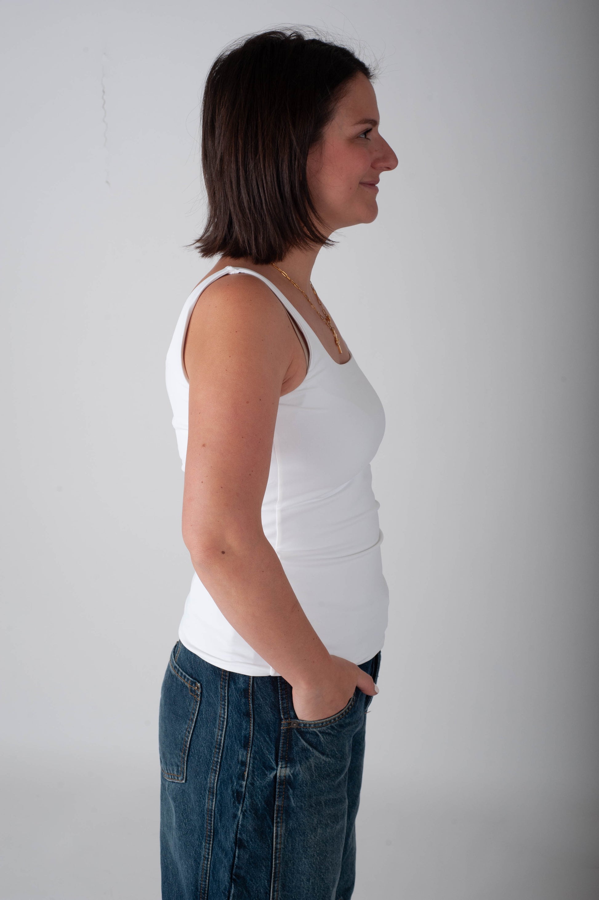 Woman wearing a white tank top and blue jeans against a plain background