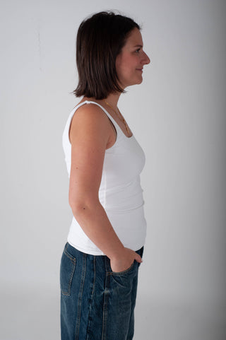 Woman wearing a white tank top and blue jeans against a plain background