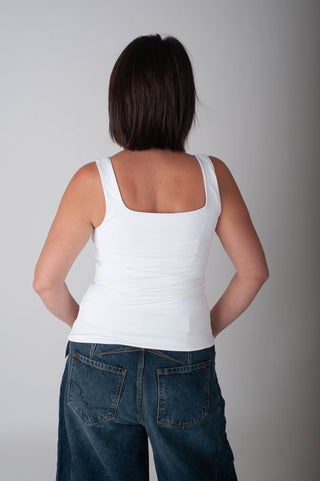 Person wearing a white tank top and blue jeans against a plain background