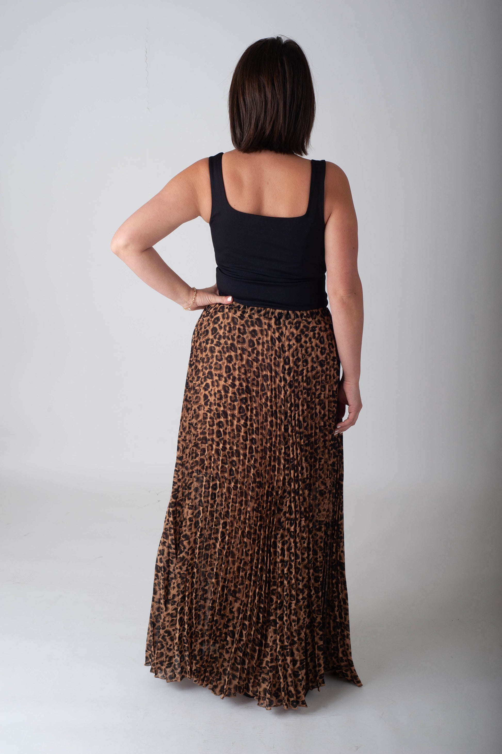 Person wearing a black tank top and leopard print skirt on a plain background