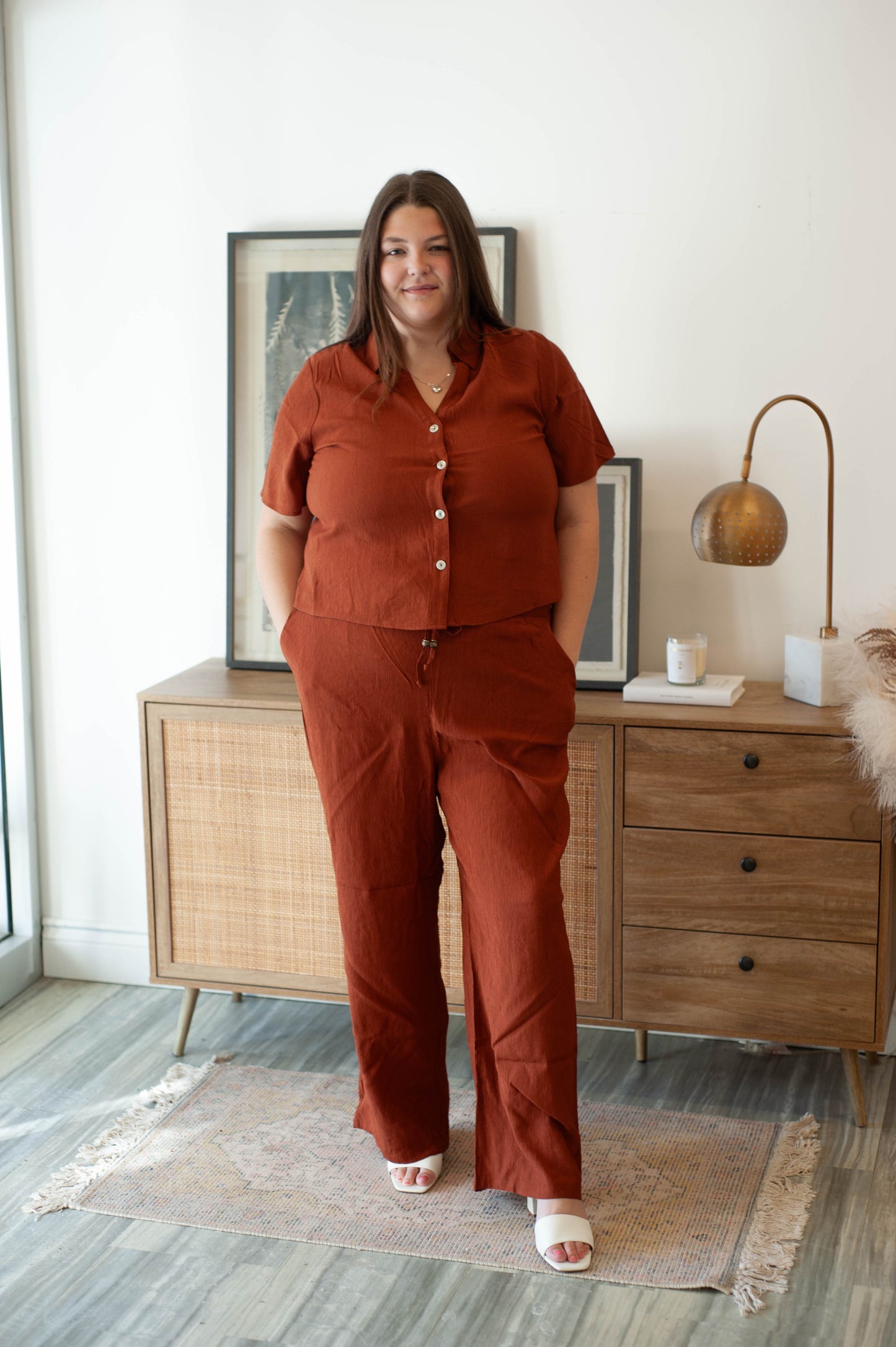 Woman in a rust-colored outfit standing in a room with wooden furniture and decor.