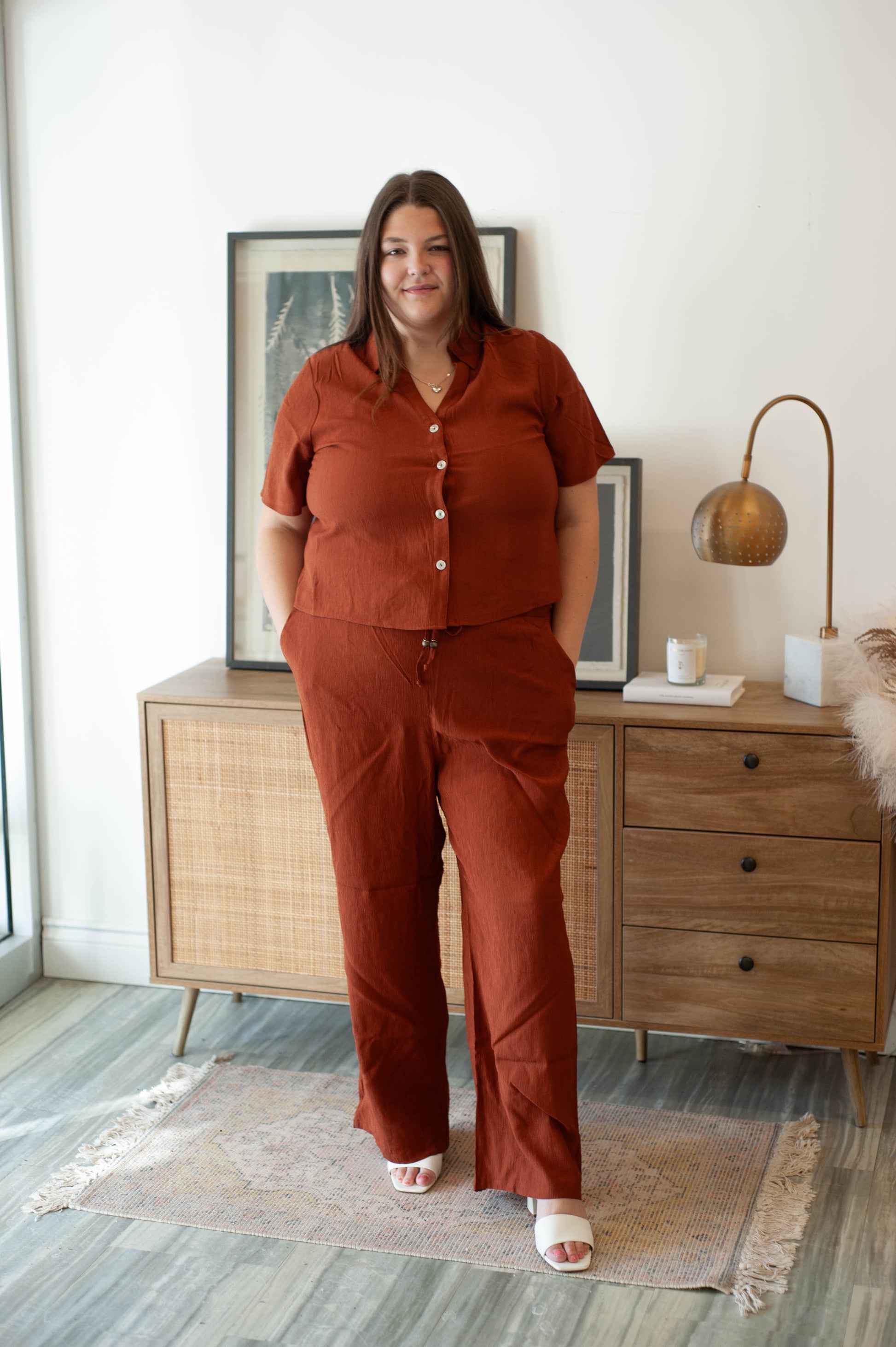 Woman in a rust-colored outfit standing in a room with wooden furniture and decor.