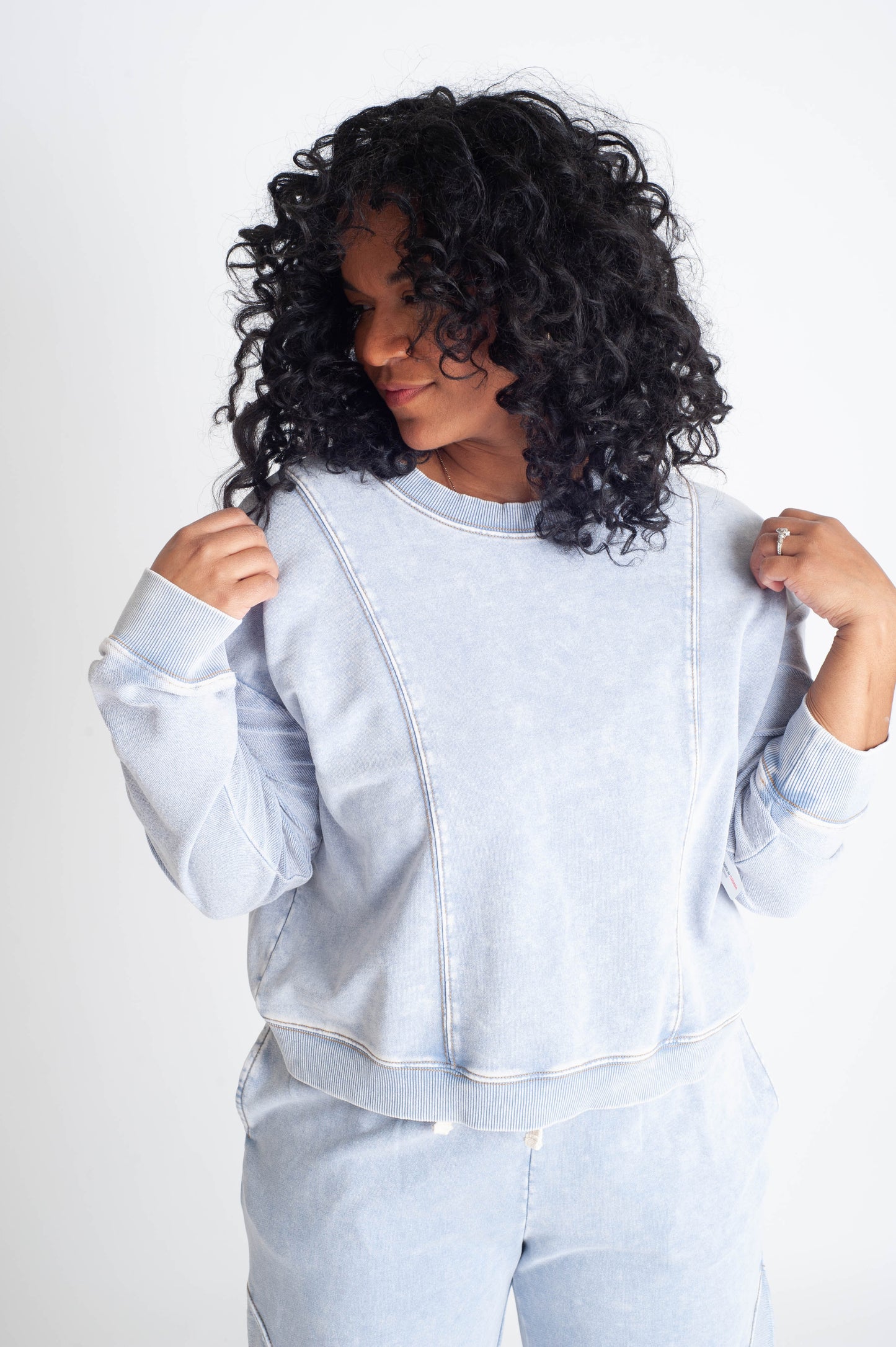 Woman wearing a light blue sweatshirt and pants set against a white background