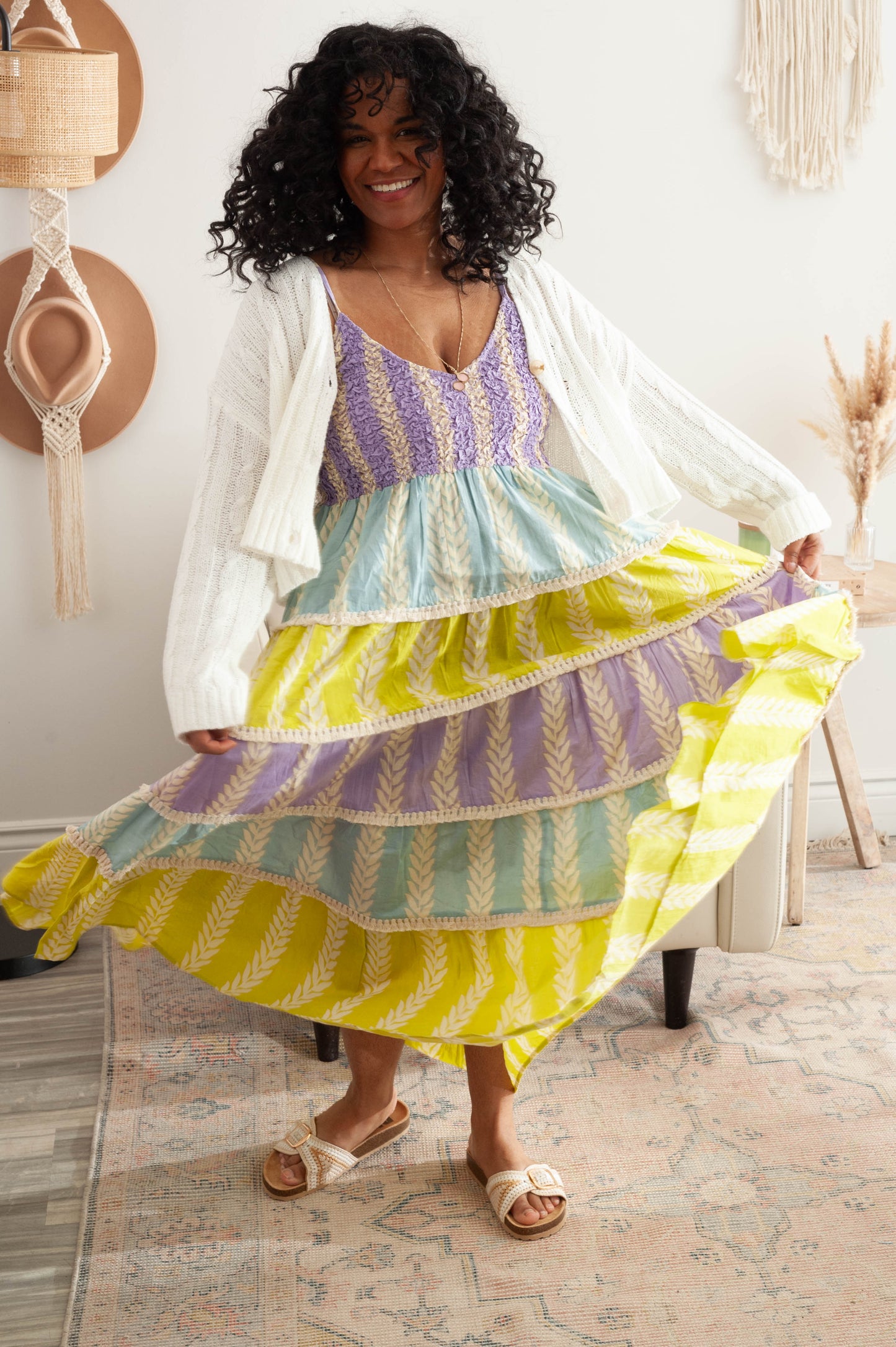Woman wearing a colorful striped dress with a white cardigan in a home setting.