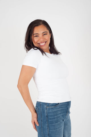 Woman wearing a white t-shirt and blue jeans against a plain background