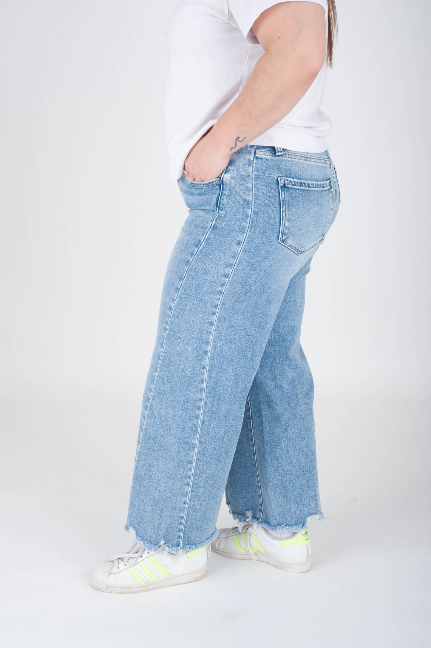 Person wearing light blue jeans and white sneakers on a white background