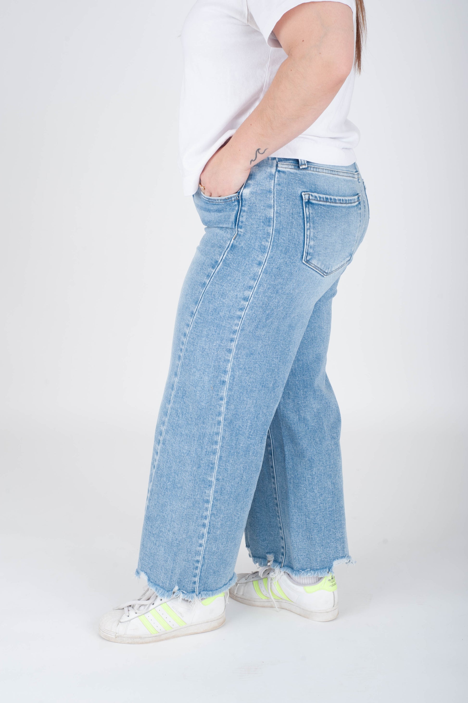 Person wearing light blue jeans and white sneakers on a white background