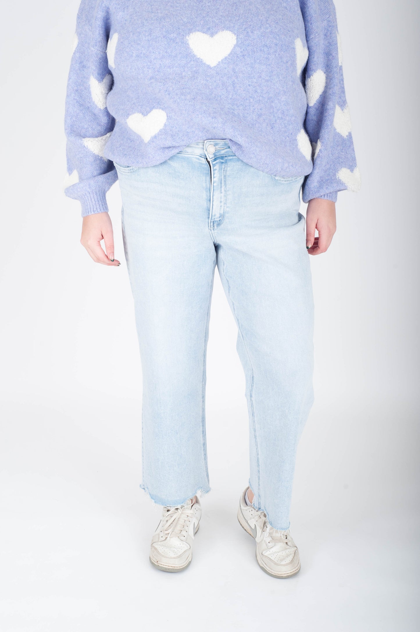 Person wearing a light blue sweater with heart patterns and light blue jeans on a white background