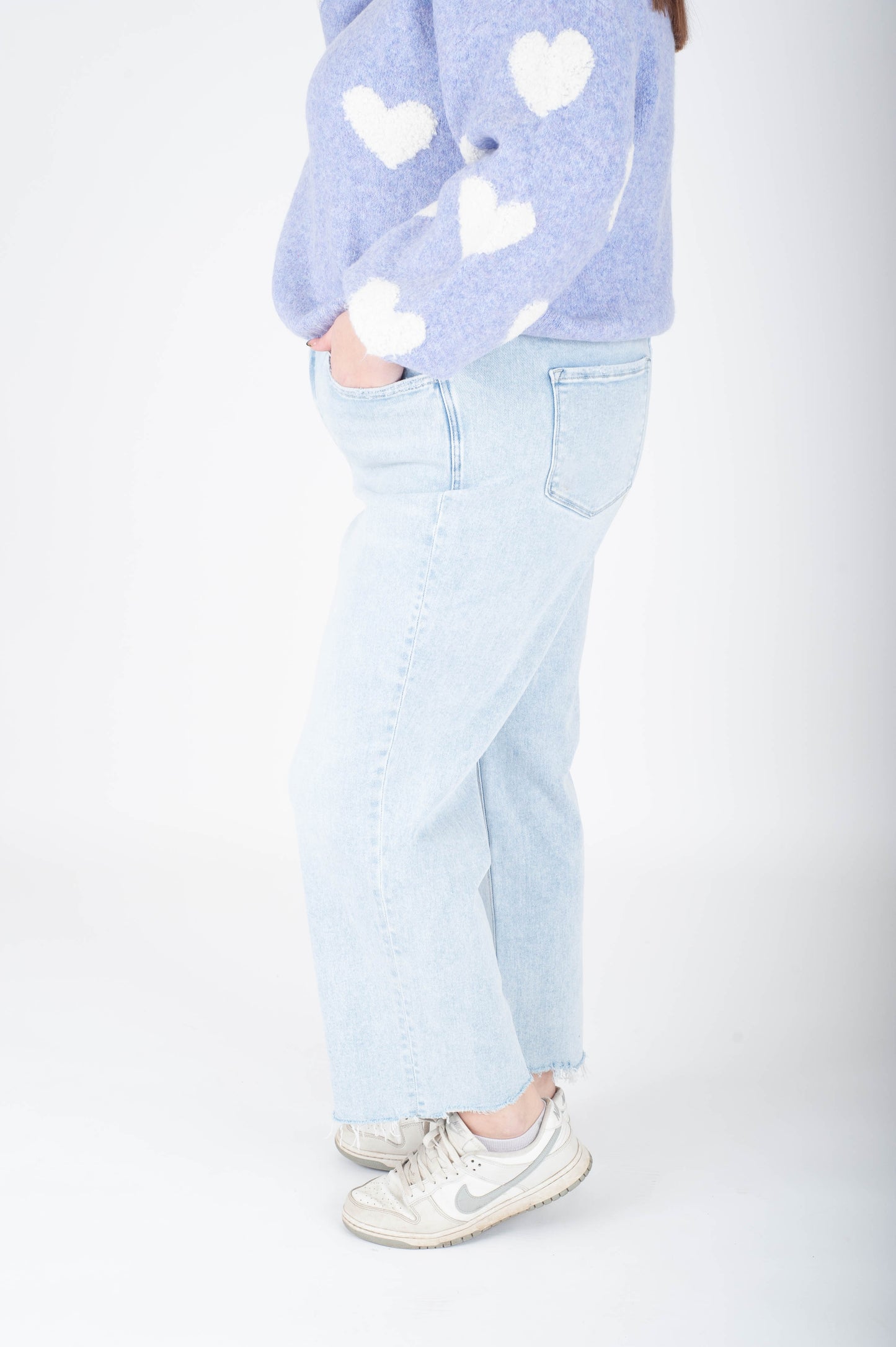 Person wearing a light blue heart-patterned sweater and light blue jeans on a white background