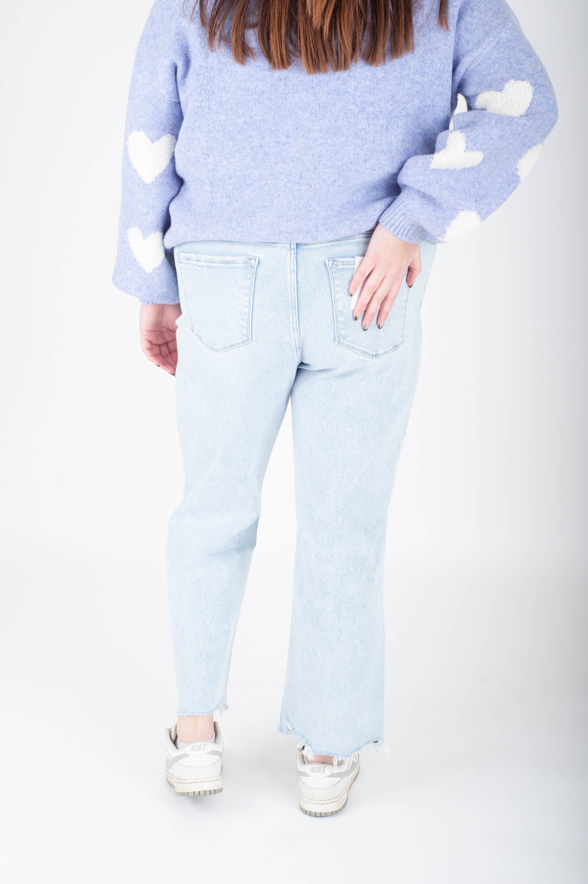 Person wearing a light blue sweater with heart cutouts and light blue jeans on a white background