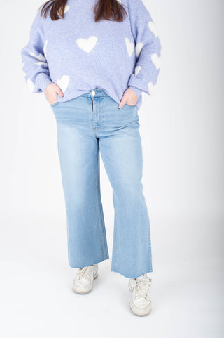 Person wearing a light blue sweater with heart patterns and light blue jeans on a white background