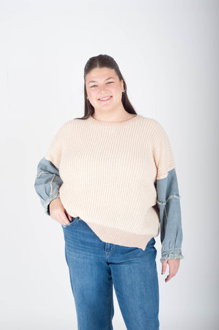 Person wearing a beige sweater with denim sleeves and blue jeans on a white background