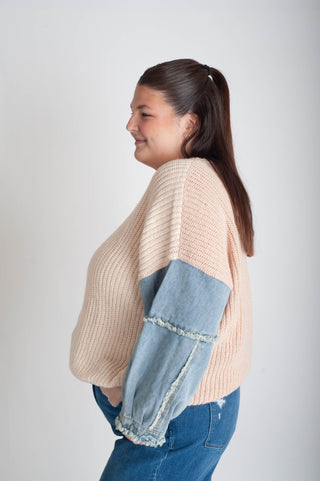 Woman wearing a beige sweater with denim sleeves on a plain background