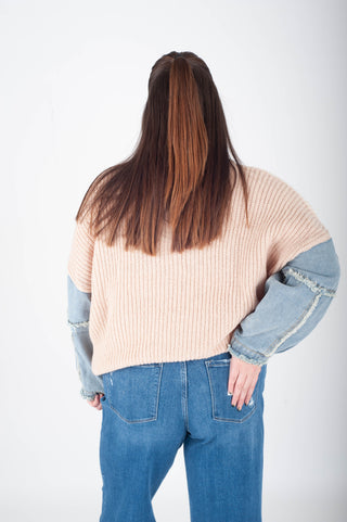 Person wearing a beige sweater with denim sleeves and blue jeans on a white background