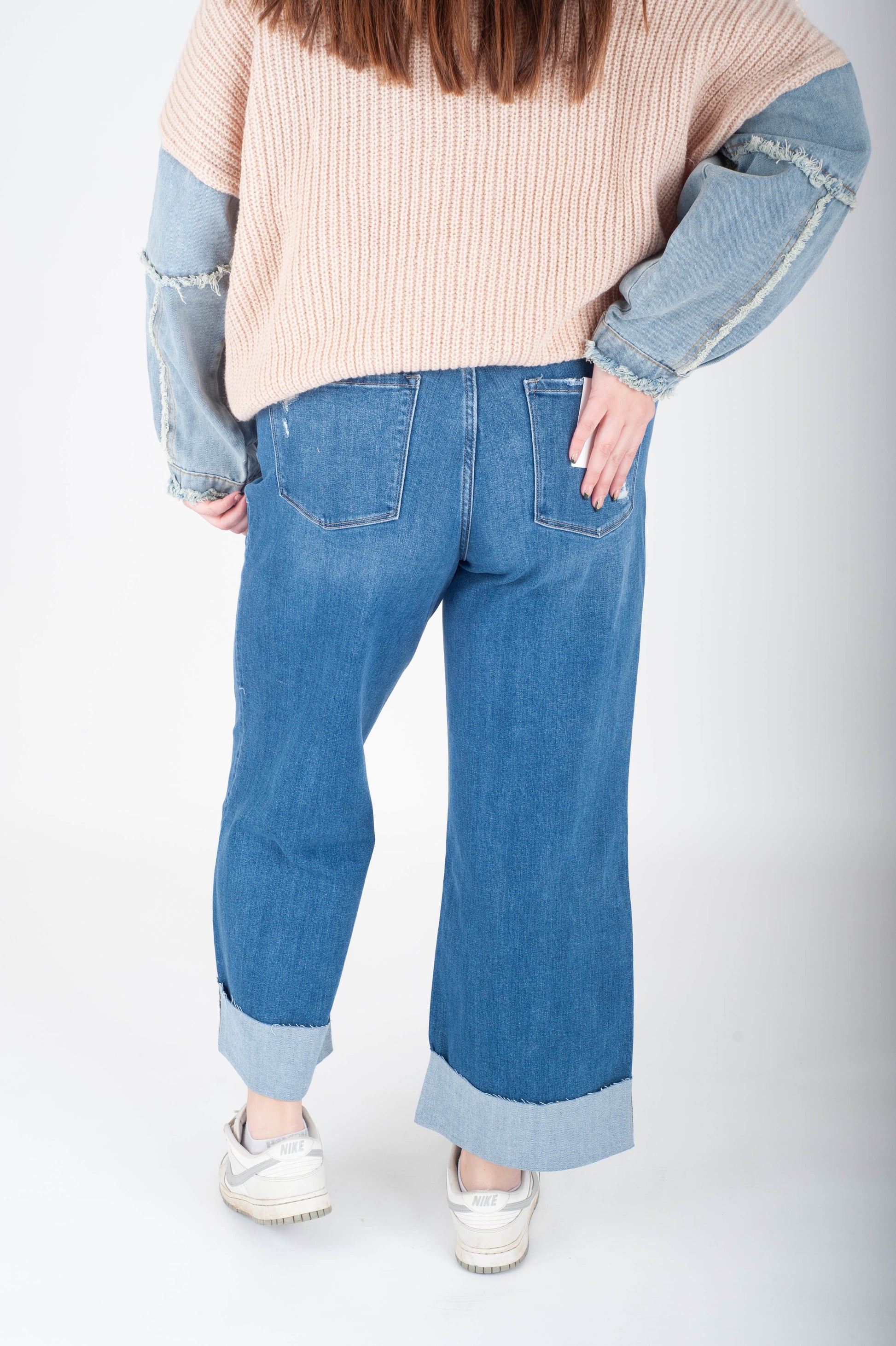 Person wearing a beige sweater with blue sleeves and blue jeans on a white background