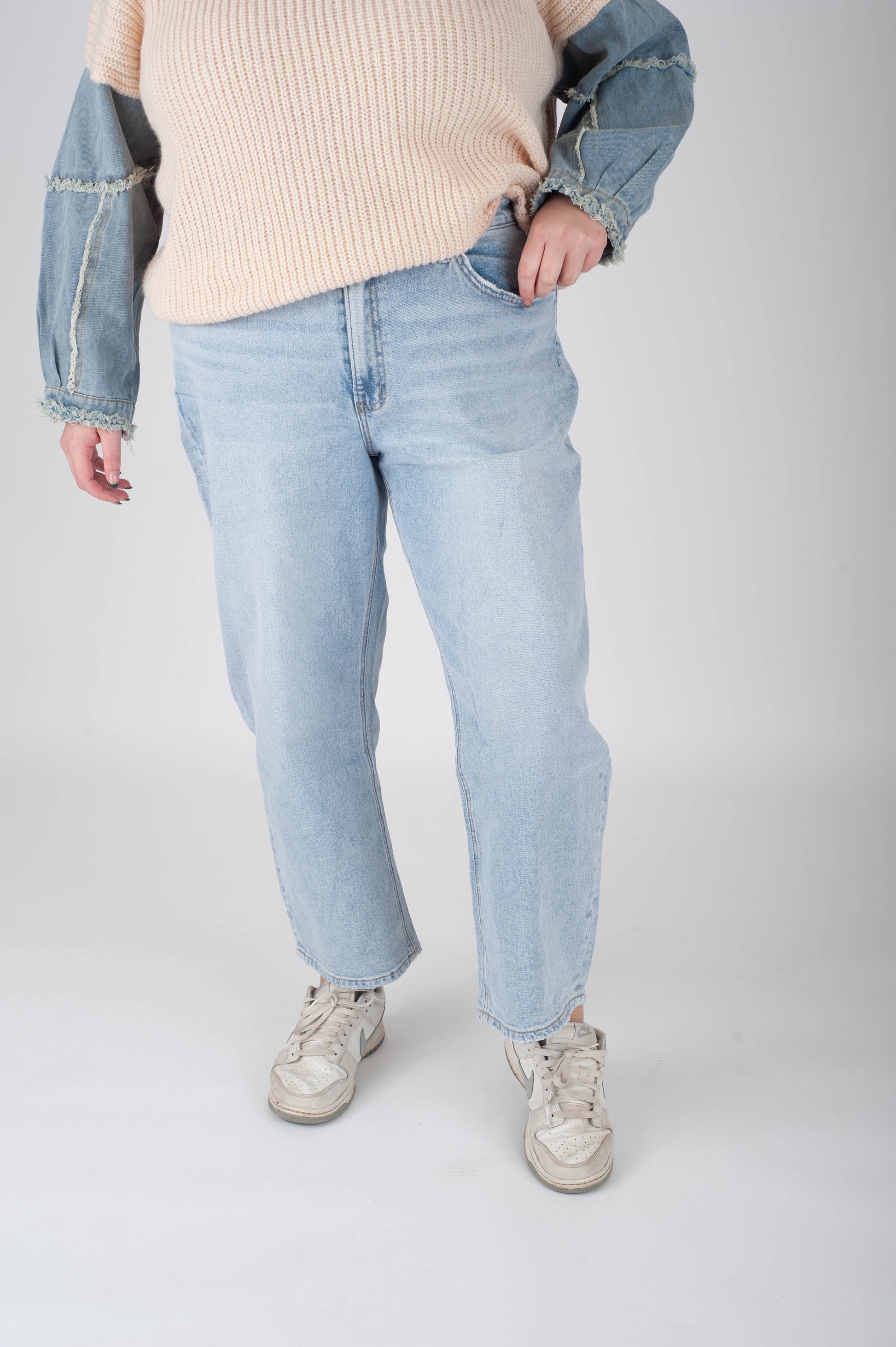 Person wearing light blue jeans and a beige sweater with a denim jacket on a white background