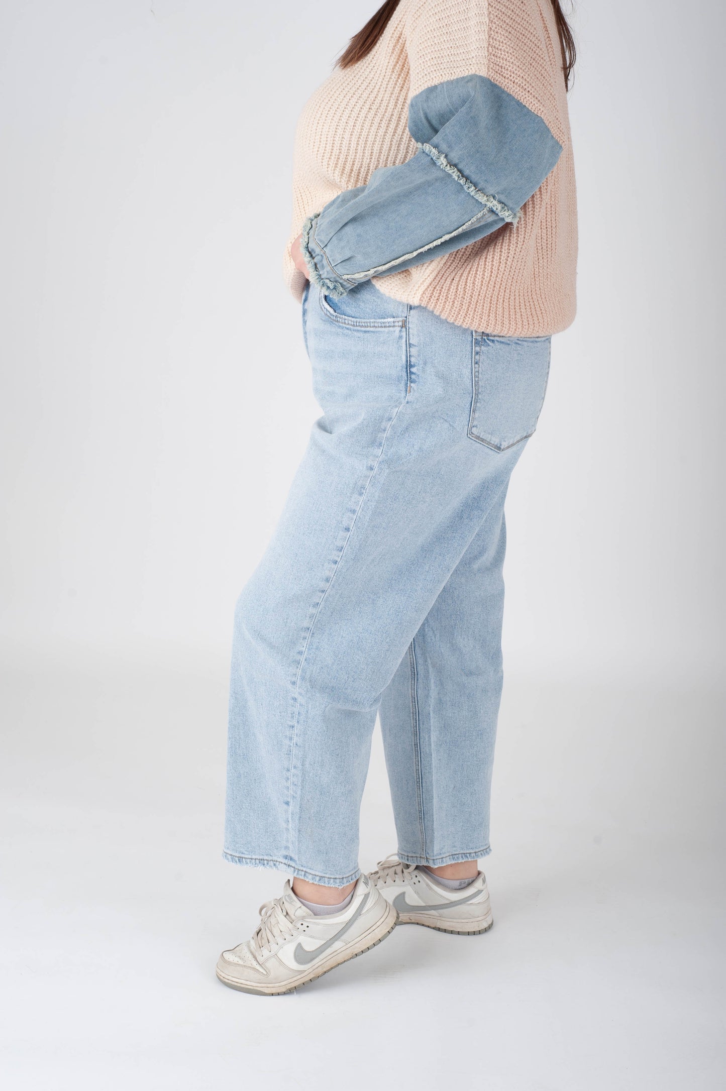 Person wearing light blue jeans and a beige sweater on a white background