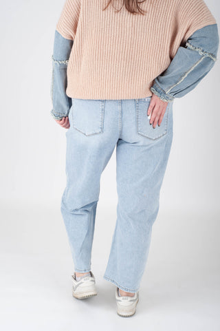 Person wearing light blue jeans and a beige sweater with denim sleeves on a white background