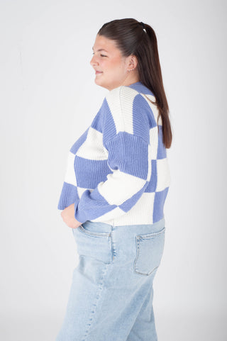 Person wearing a blue and white checkered sweater with light blue jeans on a plain background
