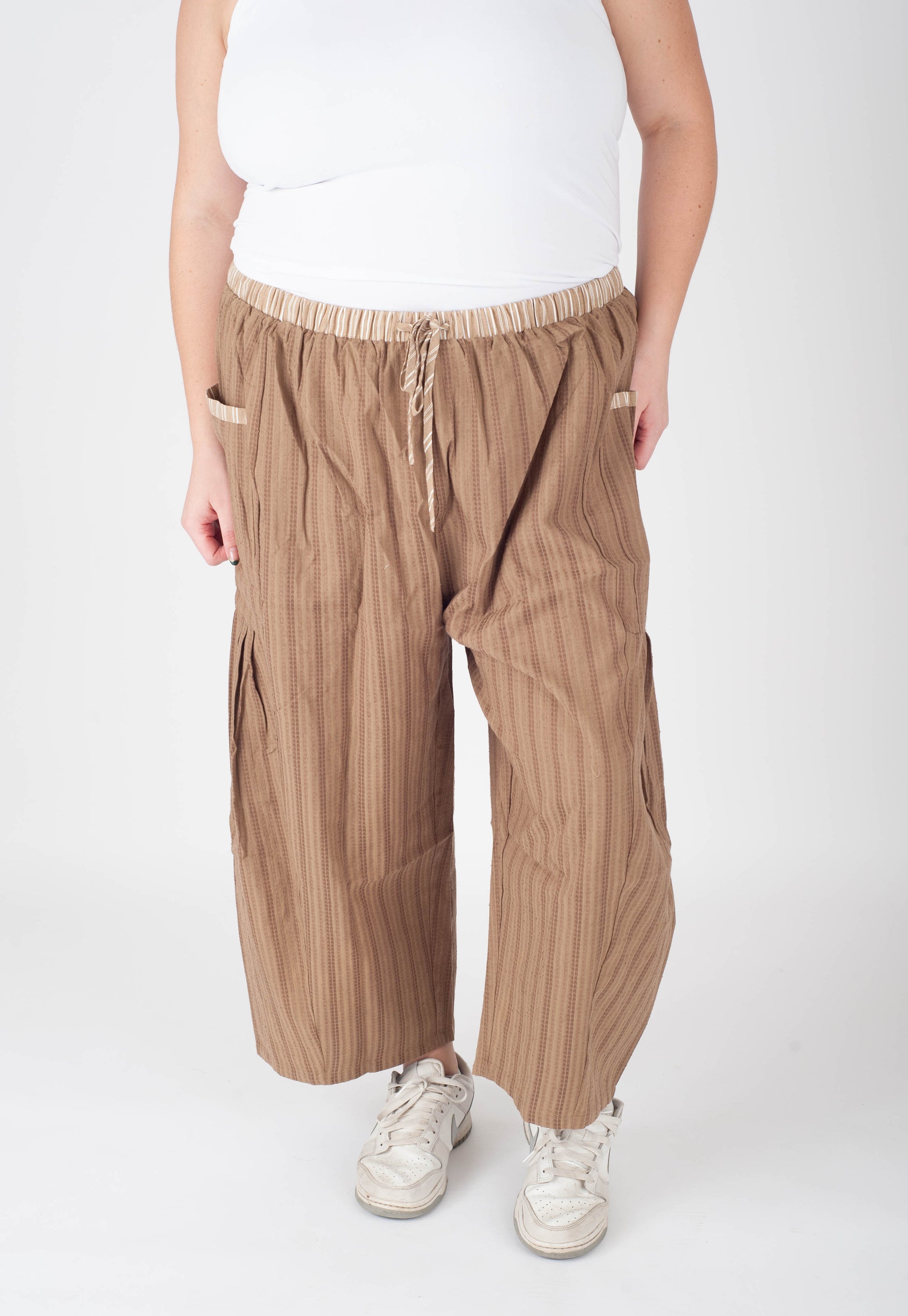 Person wearing brown striped pants and white sneakers on a white background