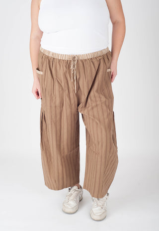 Person wearing brown striped pants and white sneakers on a white background