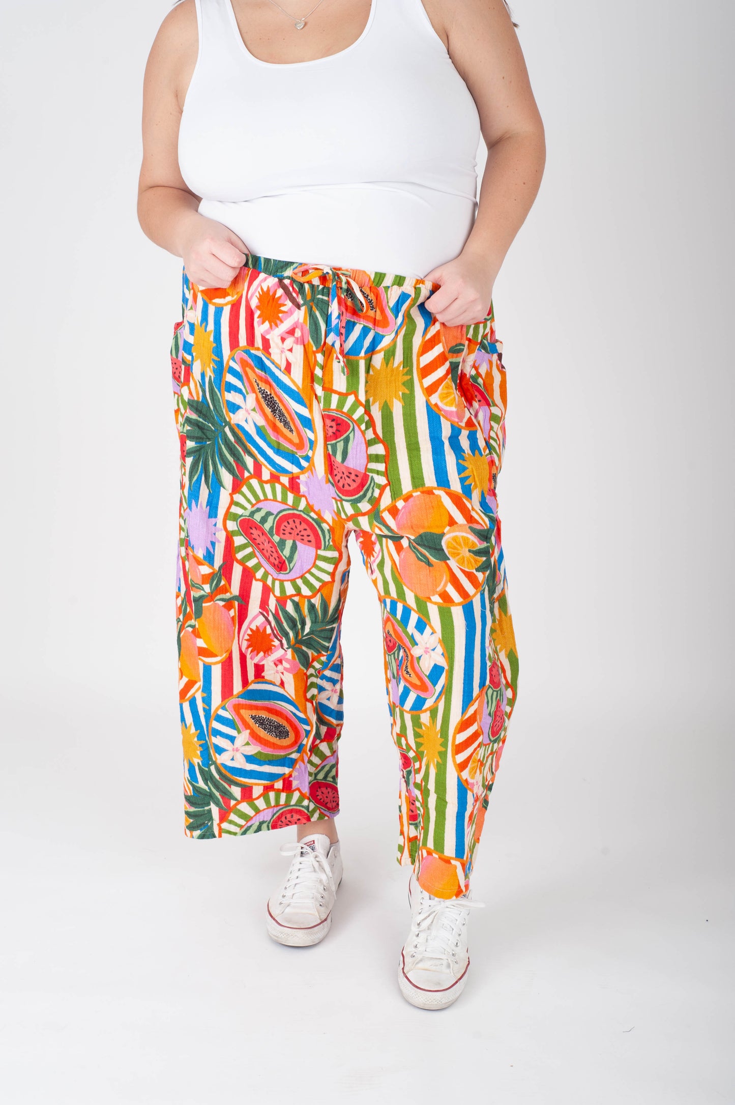Person wearing colorful tropical print pants and white sneakers on a white background