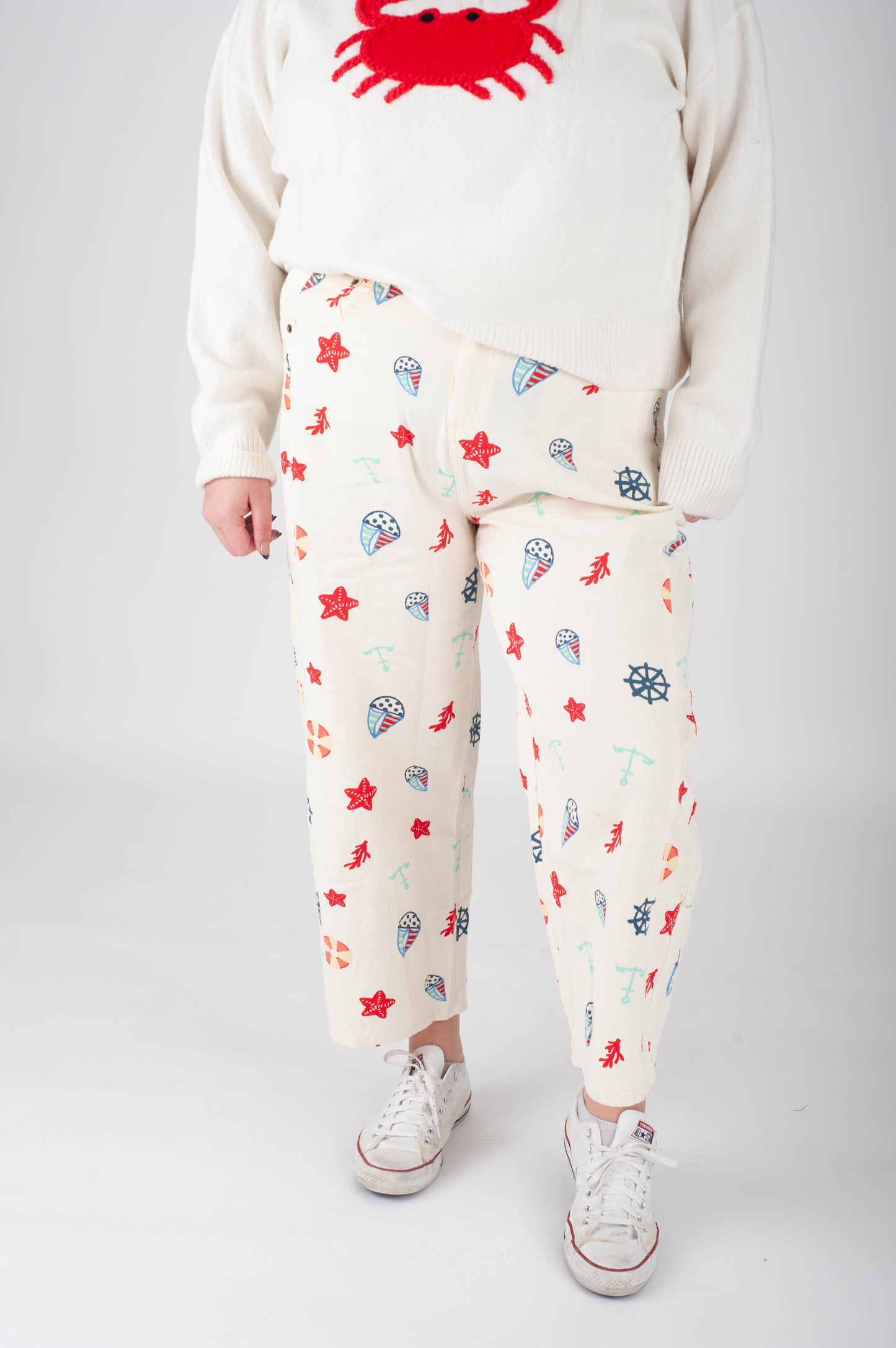 Person wearing a white sweatshirt with a red crab design and patterned pants on a plain background