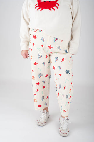 Person wearing a white sweatshirt with a red crab design and patterned pants on a plain background
