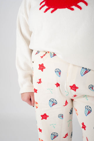 Person wearing a white sweater with a red crab design and patterned pants on a gray background