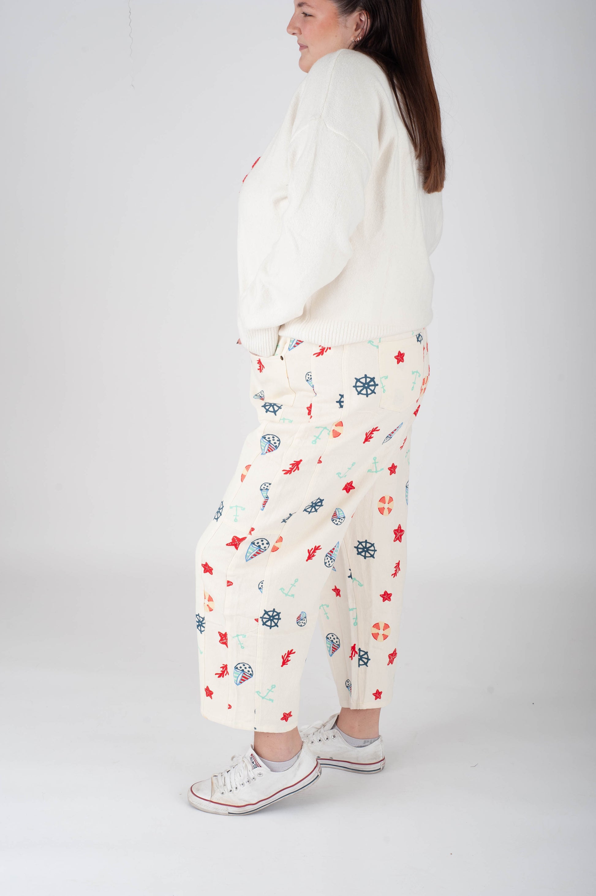 Person wearing a white sweater and floral pants on a plain background