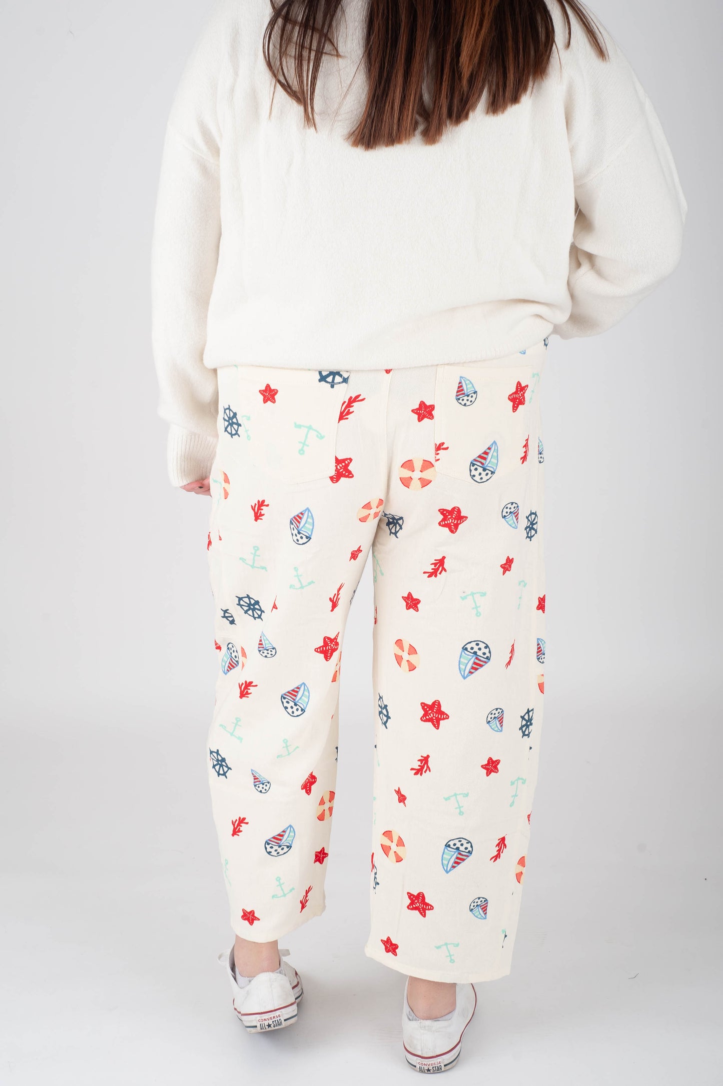 Person wearing a white sweatshirt and floral-patterned pants on a plain background