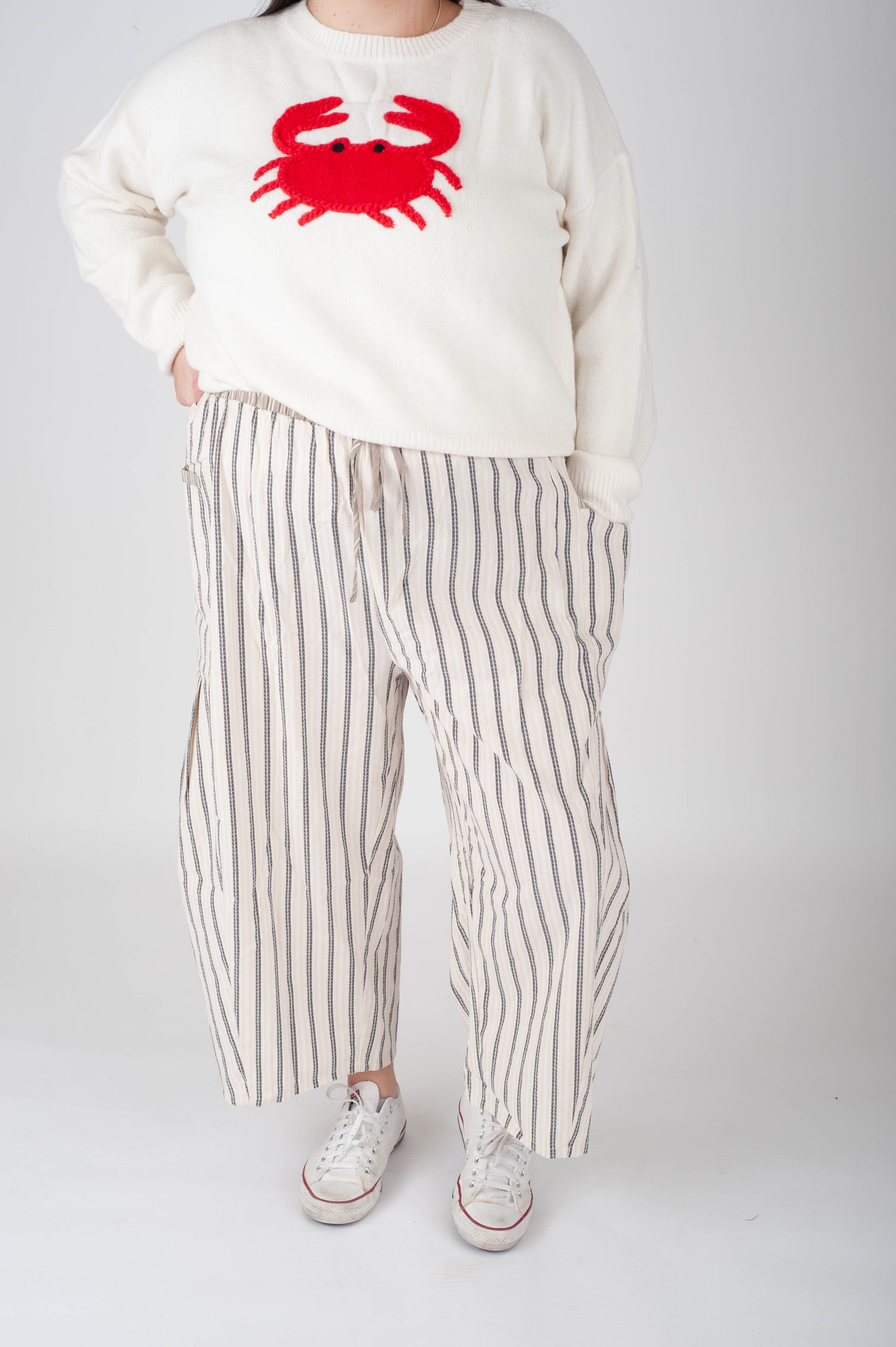 Person wearing a white sweater with a red crab design and striped pants on a plain background