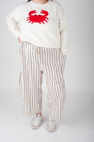 Person wearing a white sweater with a red crab design and striped pants on a plain background