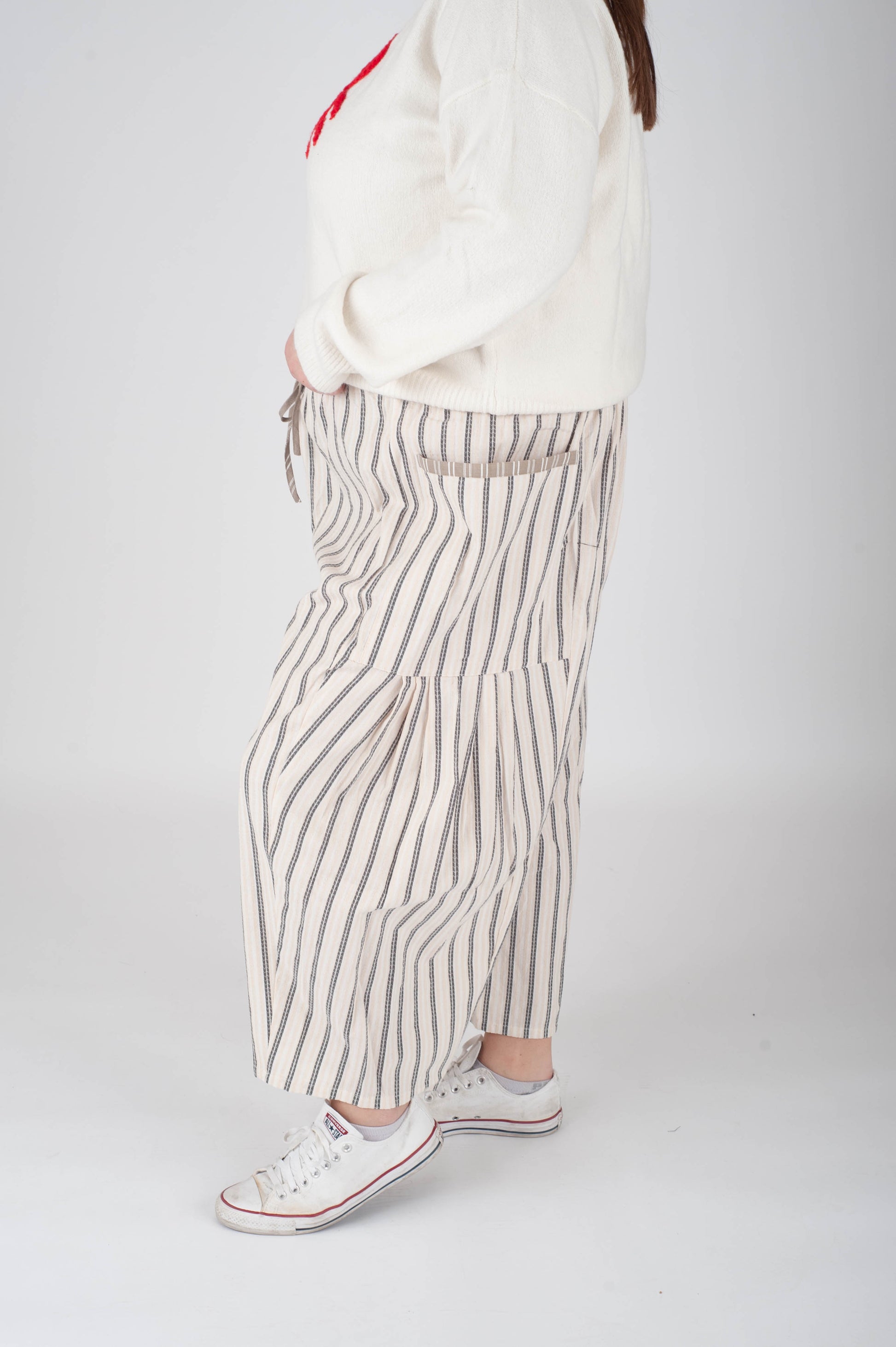 Person wearing a white shirt, striped pants, and white sneakers on a plain background